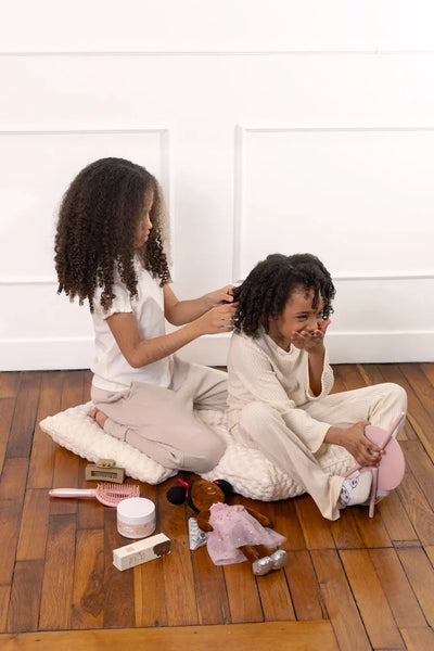 Deux filles prenant soin de leurs cheveux texturés, démêlant et nourrissant leurs boucles avec douceur et bienveillance.